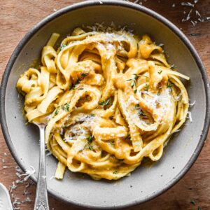 Brown bowl of fettuccini pasta with butternut squash sauce on top.