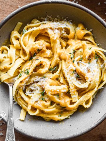 Brown bowl of fettuccini pasta with butternut squash sauce on top.