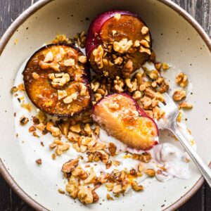 Roasted plums in a bowl with yogurt and nuts.