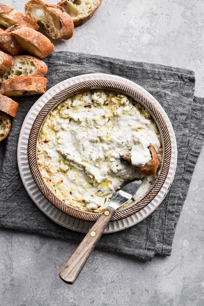 Roasted garlic baked ricotta dip in bowl with bread and spatula