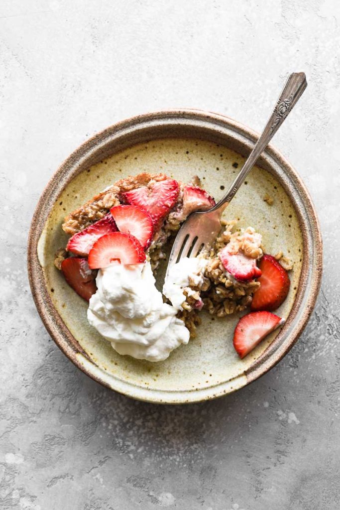 A plate of baked oatmeal with whipped cream and a bite taken out.