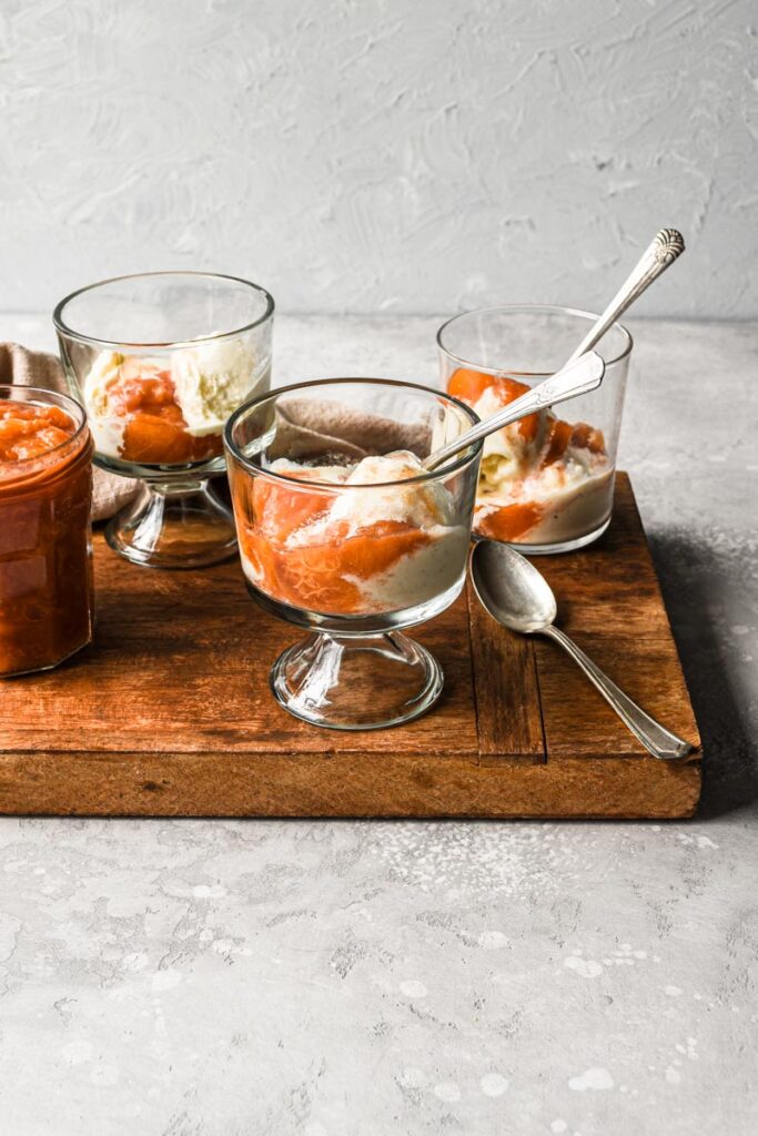 Glass serving bowls with vanilla ice cream and peach compote on top.