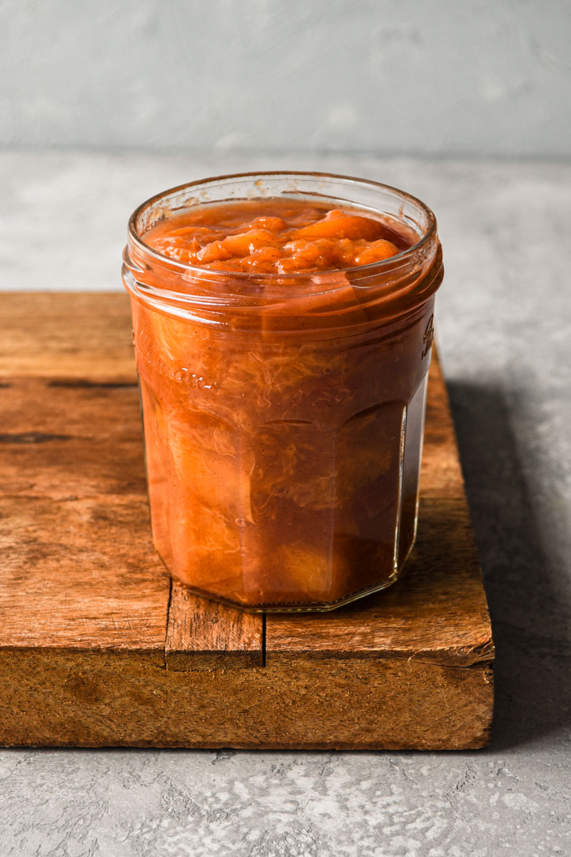 A jar of finished peach compote on a wood surface.