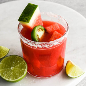 Up close image of a finished spicy watermelon margarita with watermelon slices and a salt rim.