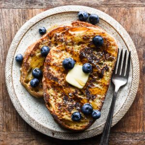 Up close of french toast with berries, syrup, and butter.