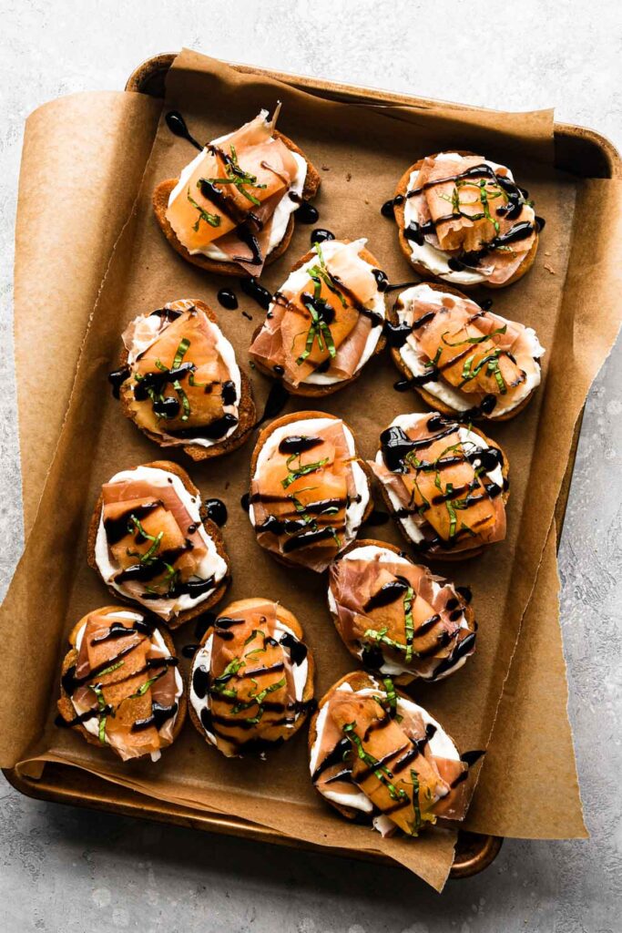 Finished crostini on a baking sheet with a drizzle of balsamic and sprinkle of basil.