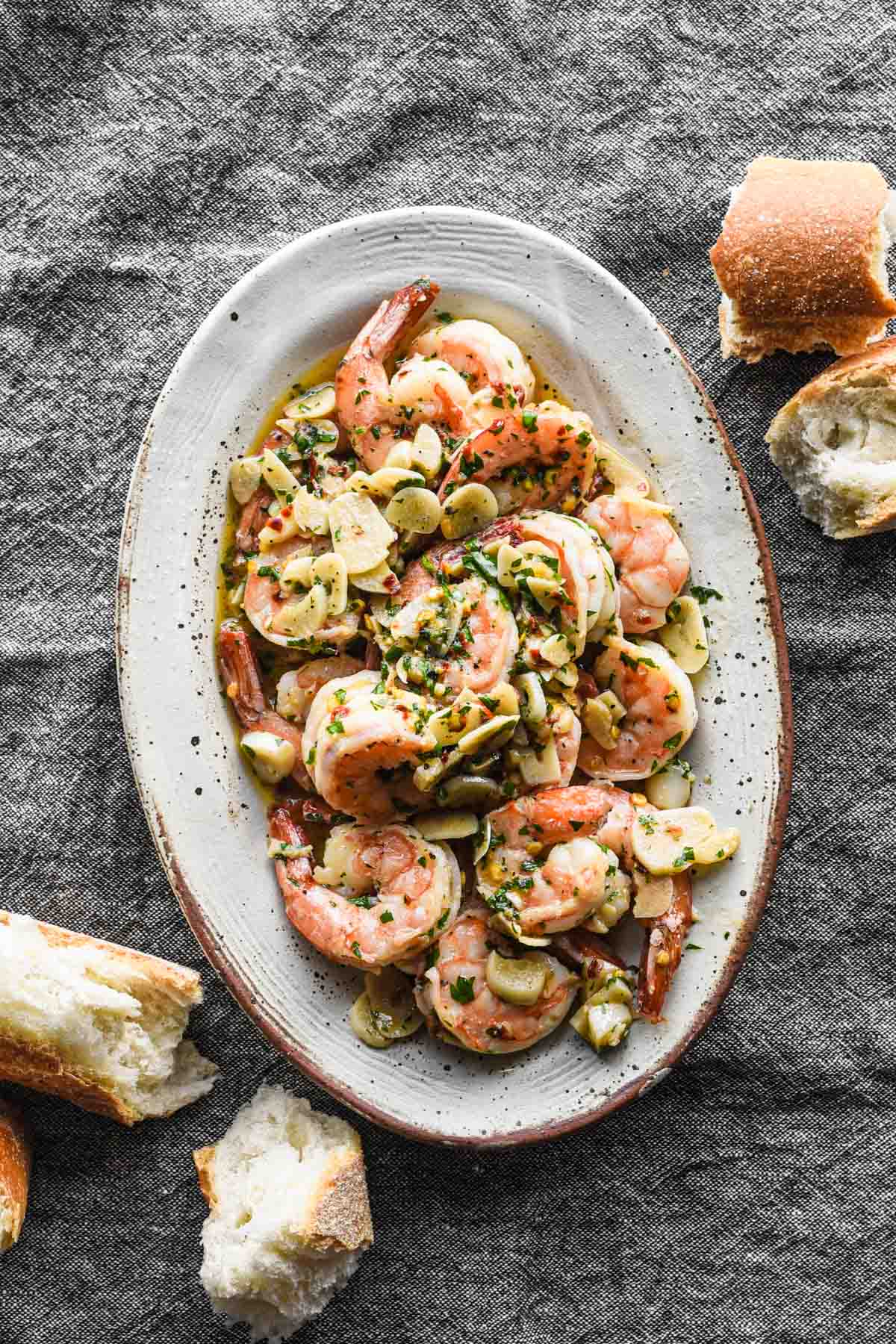 Finished spicy garlic butter shrimp on a serving platter with torn bread surrounding it. 