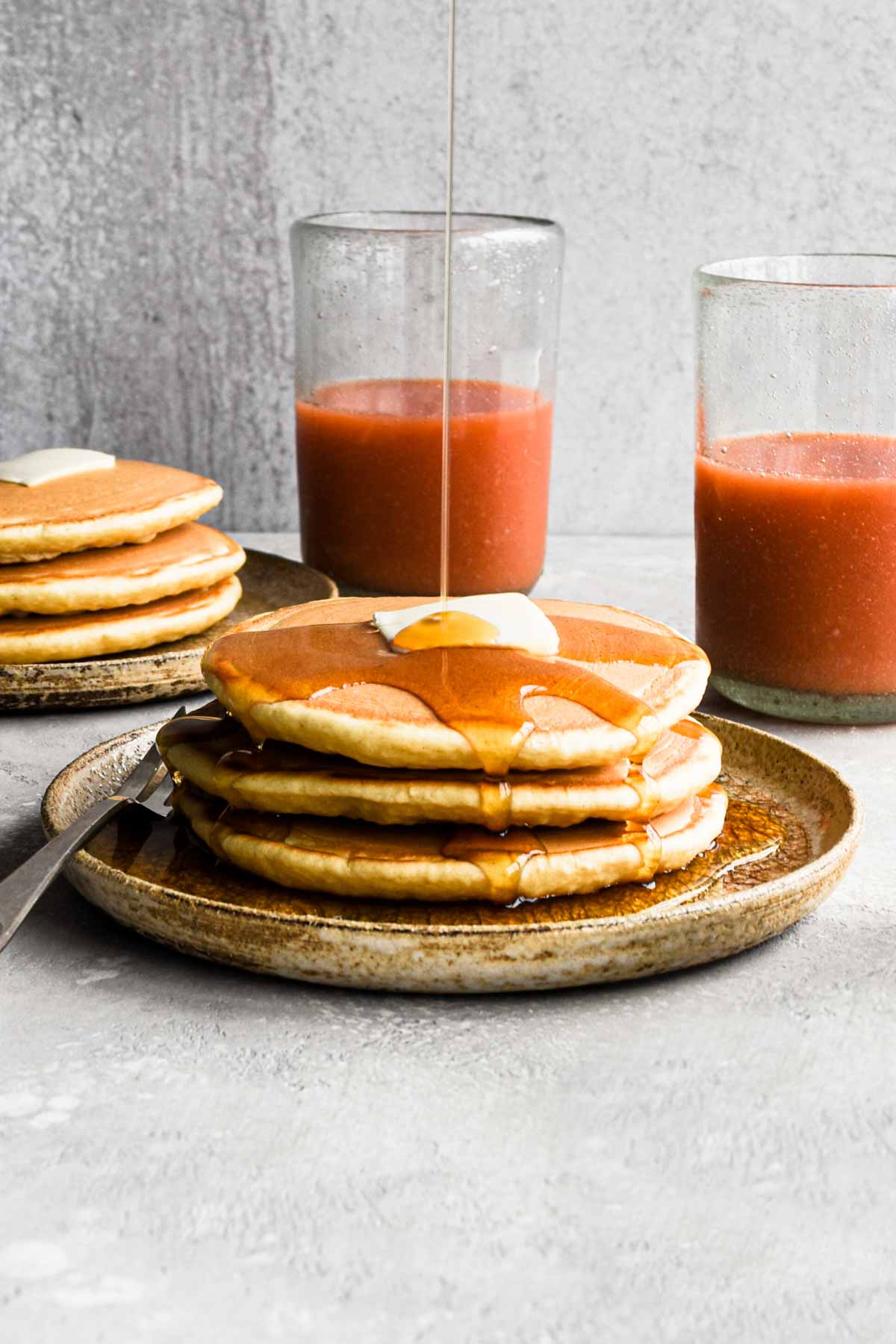 zoomed out shot of stack of pancakes with a maple syrup pour.
