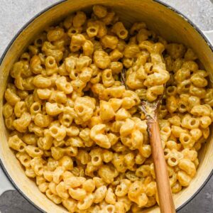 Close up shot of mac and cheese in a pot with a wood spoon.