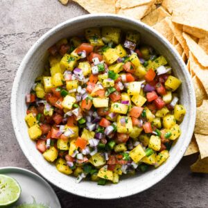 A bowl of pineapple pico de gallo with chips and limes.