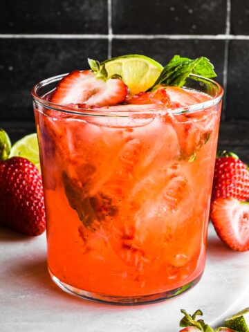 Strawberry mint margarita in a glass topped with a strawberry slice, lime, and mint.