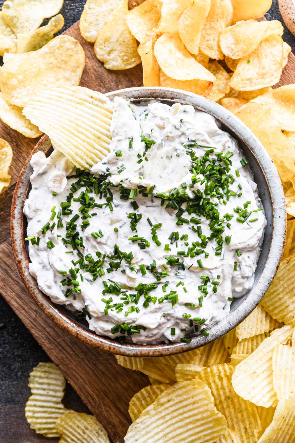 Sour cream and onion dip in a bowl with a ruffled chip dipped in.