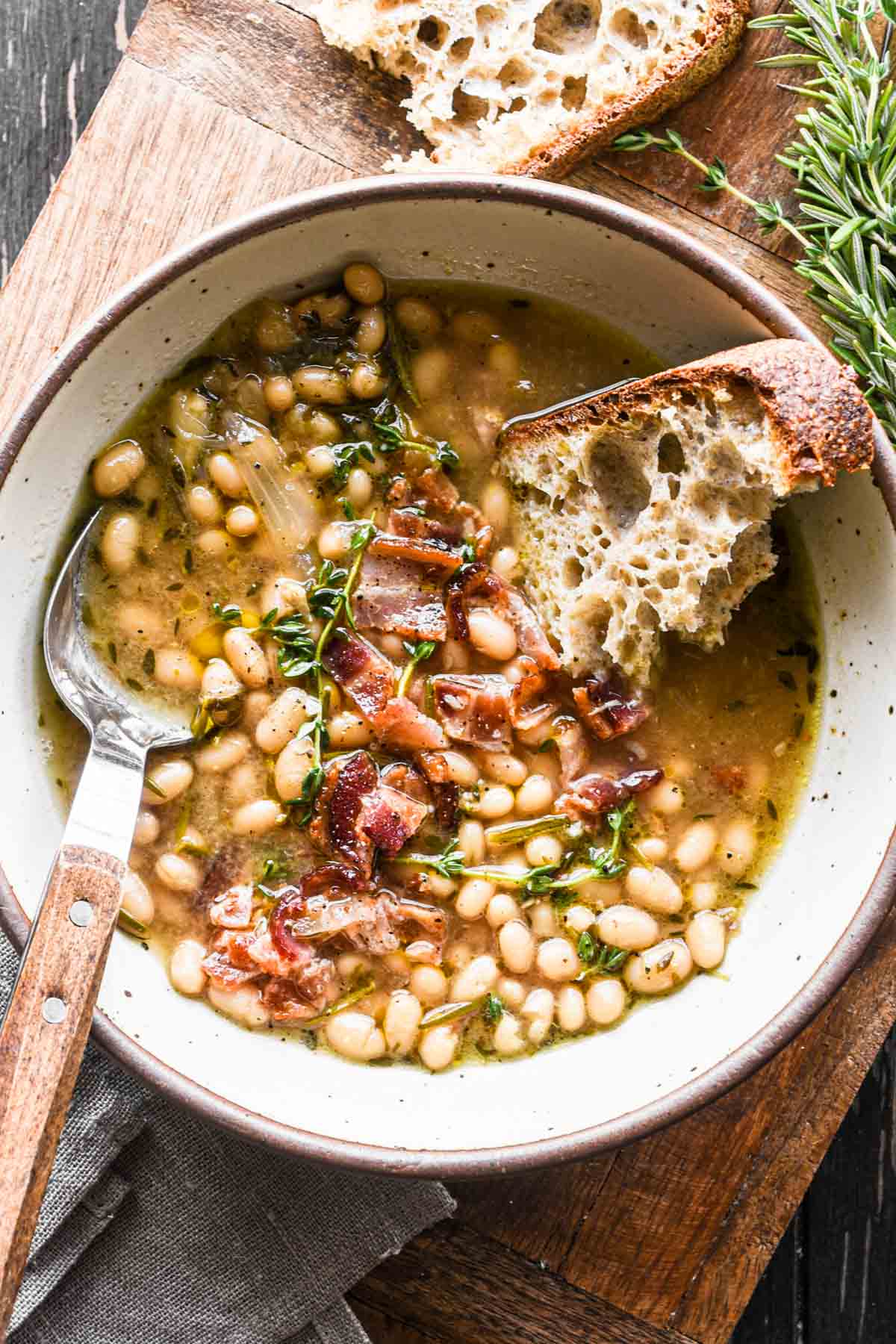 Close up image of brothy beans in a bowl topped with bacon.