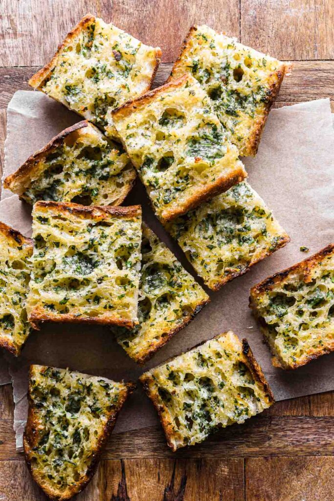 Slices of garlic bread stacked on a wood board.