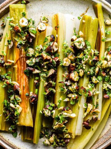 Finished braised and caramelized leeks on a serving plate with gremolata.