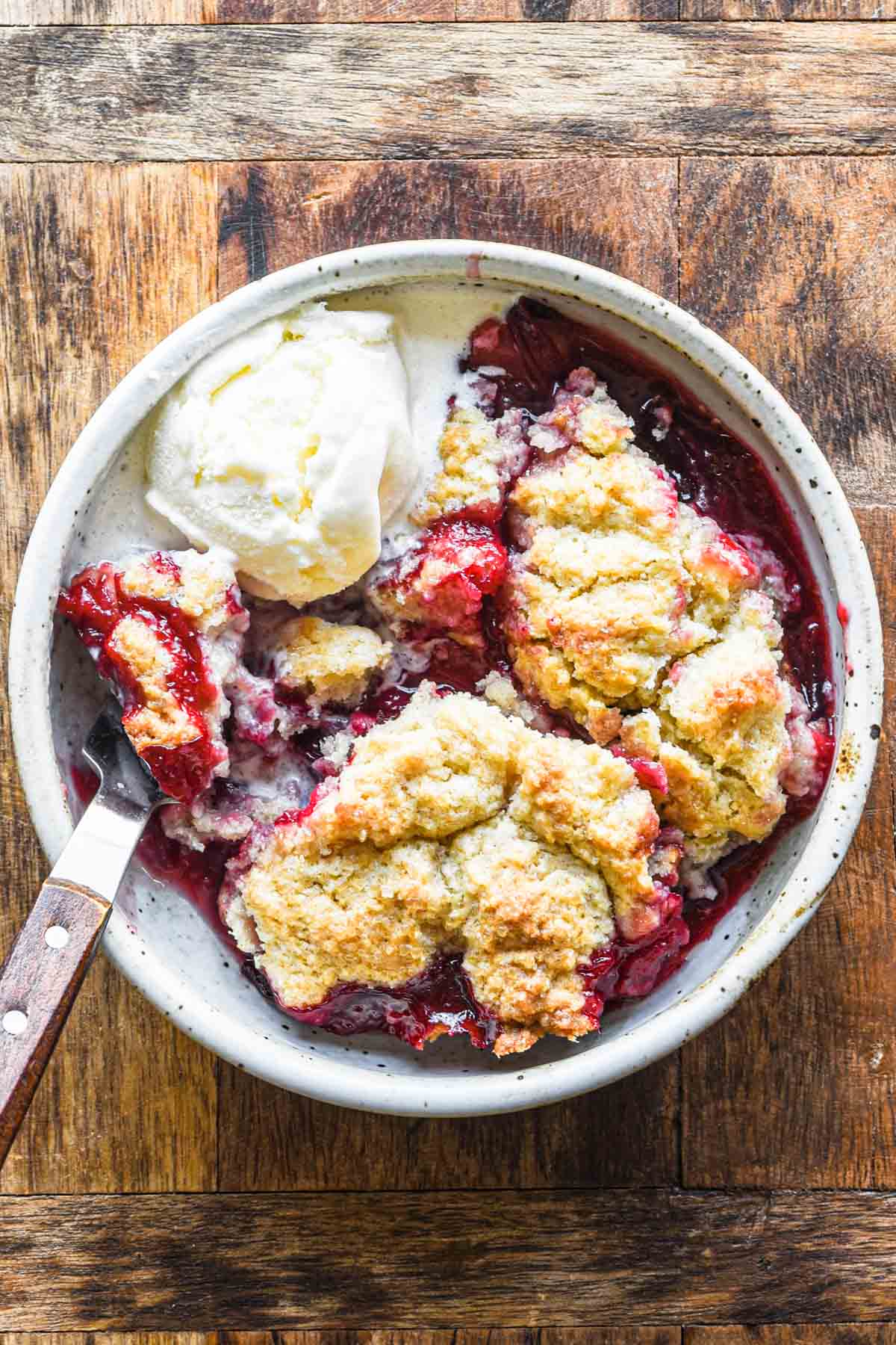 Serving of plum cobbler with ice cream in a bowl.