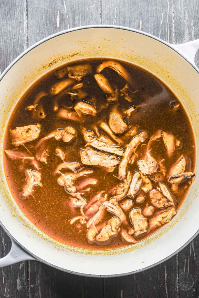 Shredding the cooked chicken and putting it back in the dutch oven.