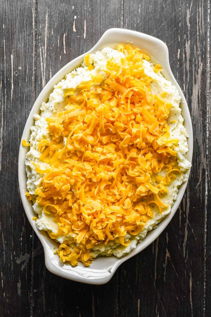 Topping the mashed potatoes with cheese in a baking dish.