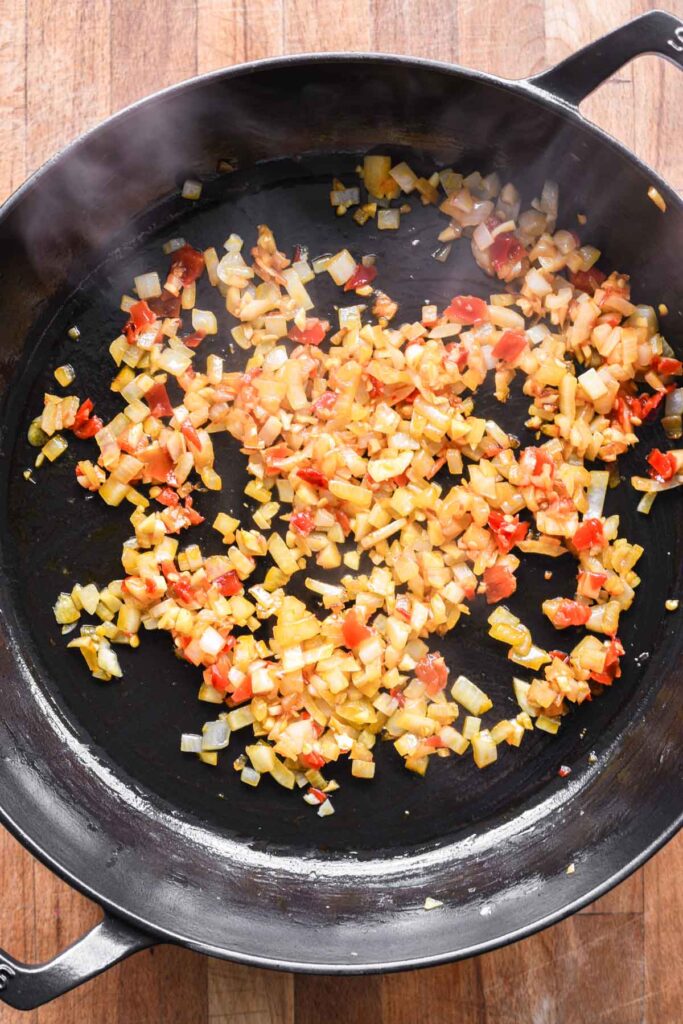 Onion, garlic, and calabrian chiles cooking in a skillet.
