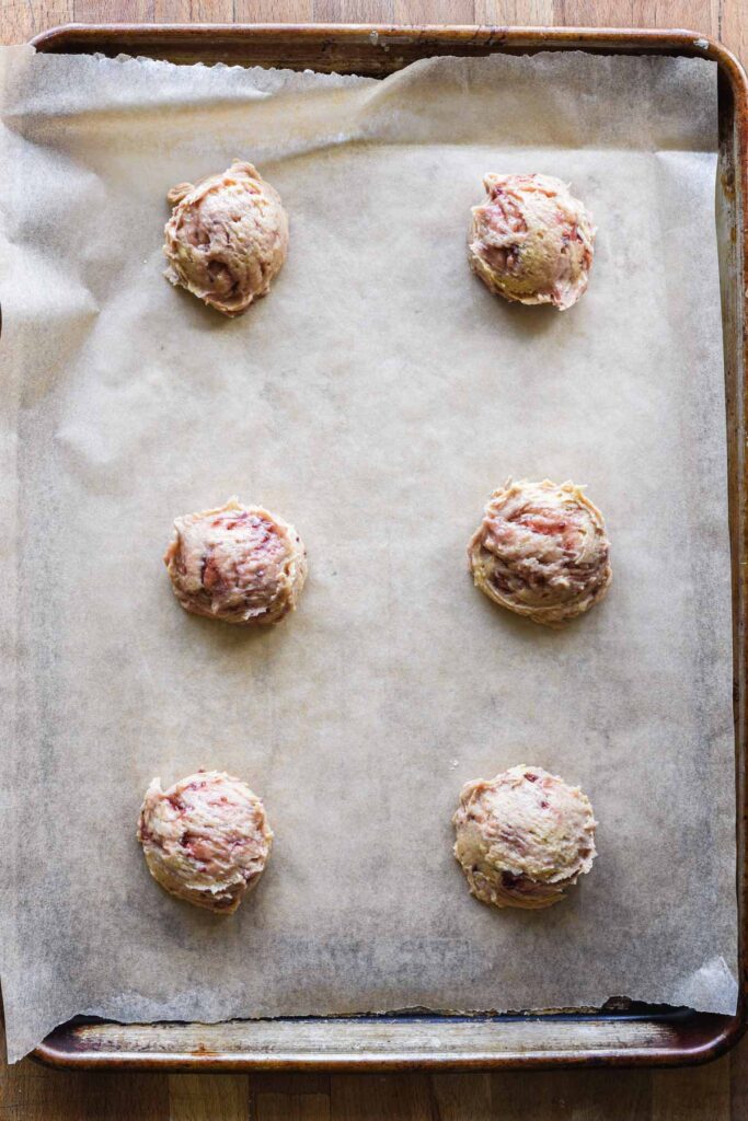 Scoops of cookie dough on a parchment lined baking sheet.