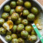 Marinated olives in a bowl with a green spoon.