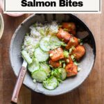 Hot honey salmon bites in a bowl with rice and marinated cucumbers.