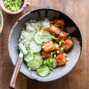 Hot honey salmon in a bowl with marinated cucumbers and rice.