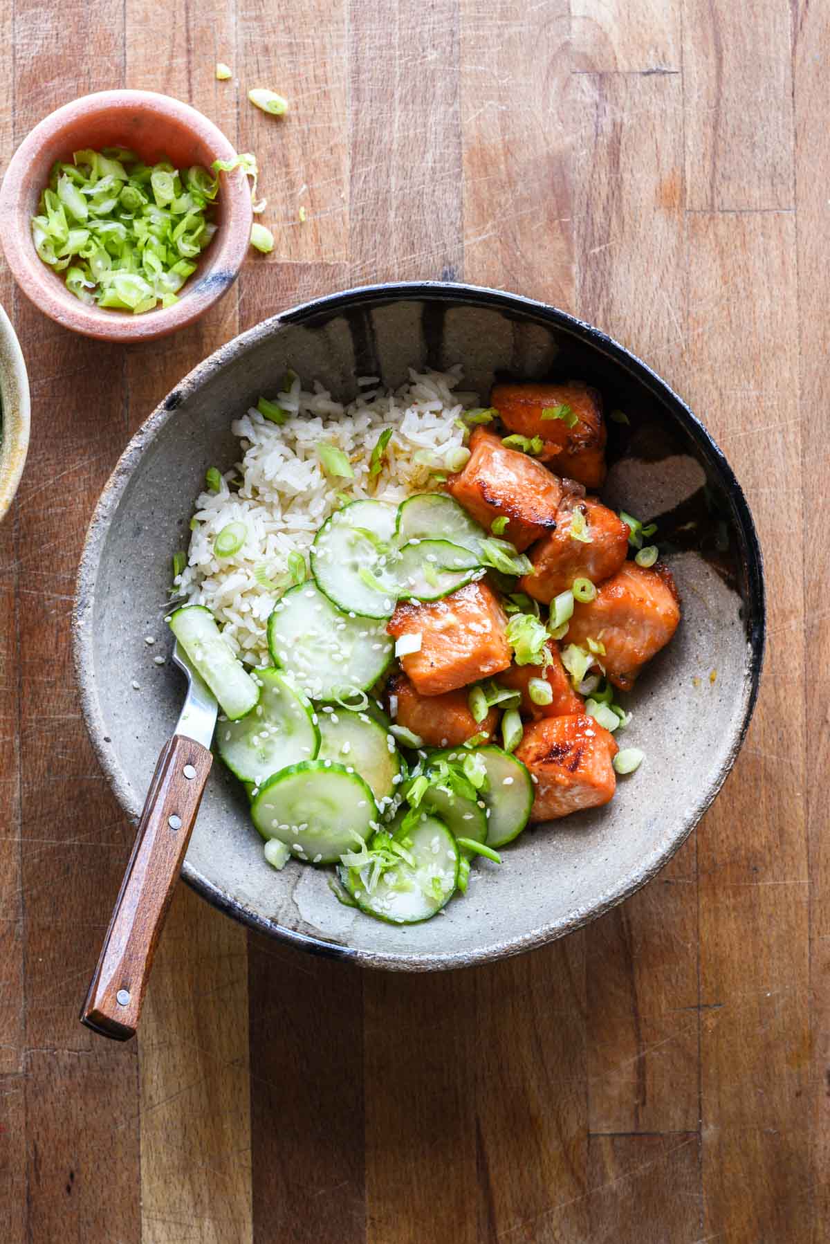 Hot honey salmon in a bowl with marinated cucumbers and rice.