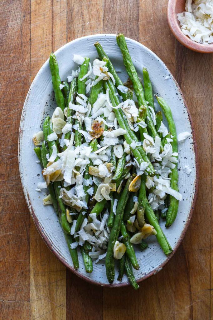 Garlic roasted green beans on a serving plate with parmesan cheese.