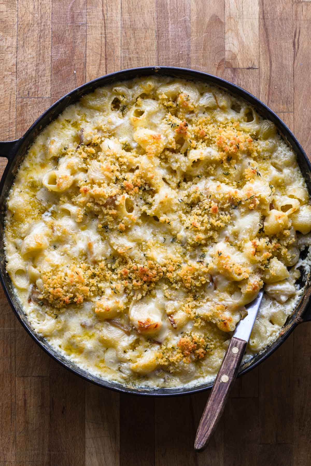 French onion mac and cheese in a skillet with a wooden spoon.