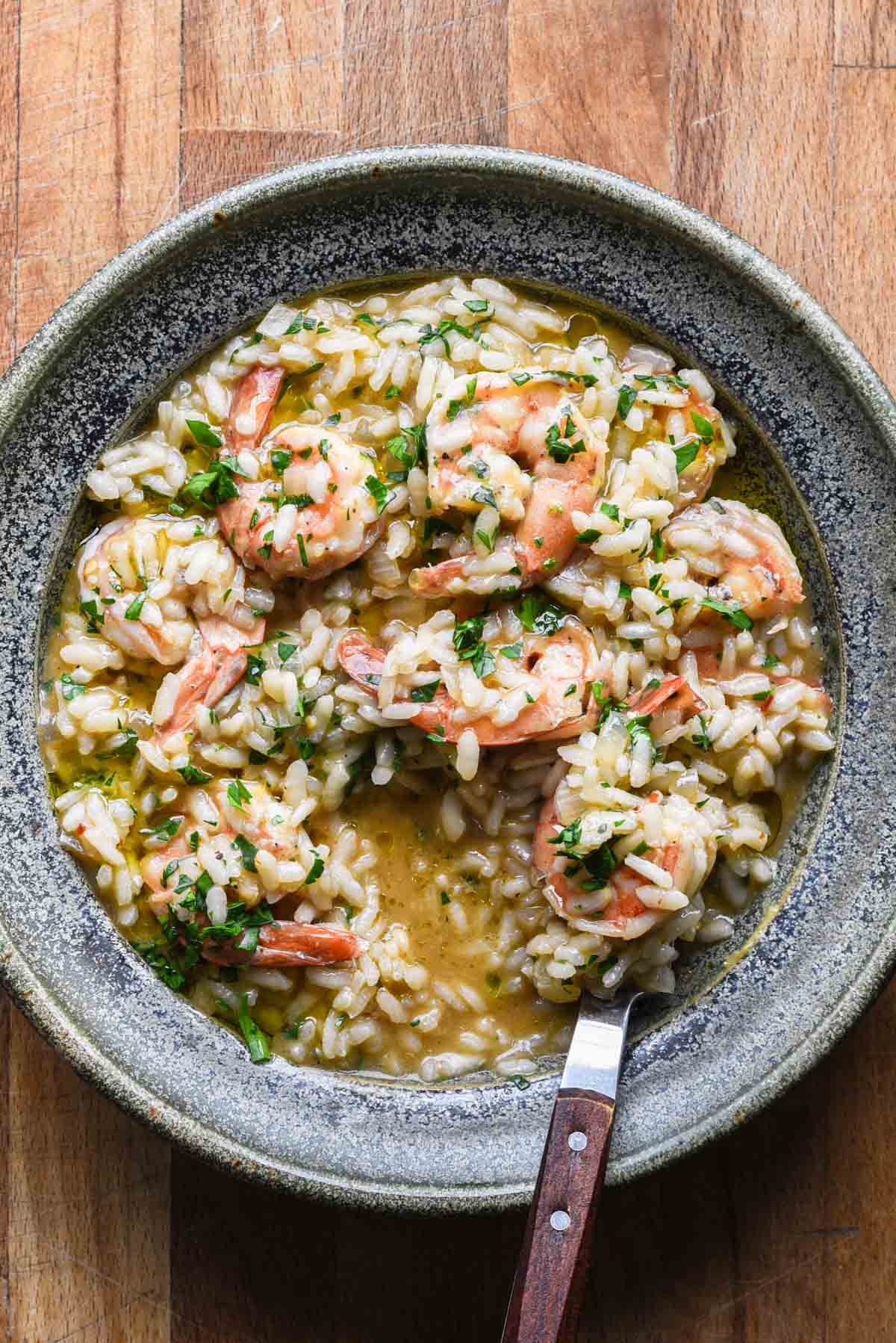 Shrimp scampi risotto in a blue bowl with a wood fork.