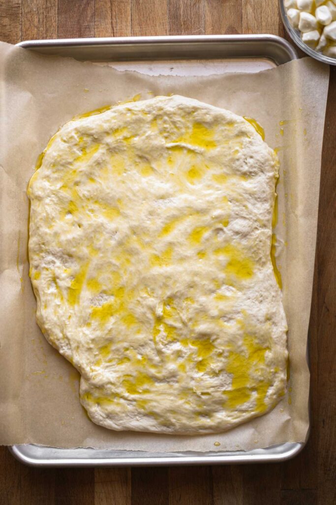 Pizza dough with olive oil on a baking sheet.