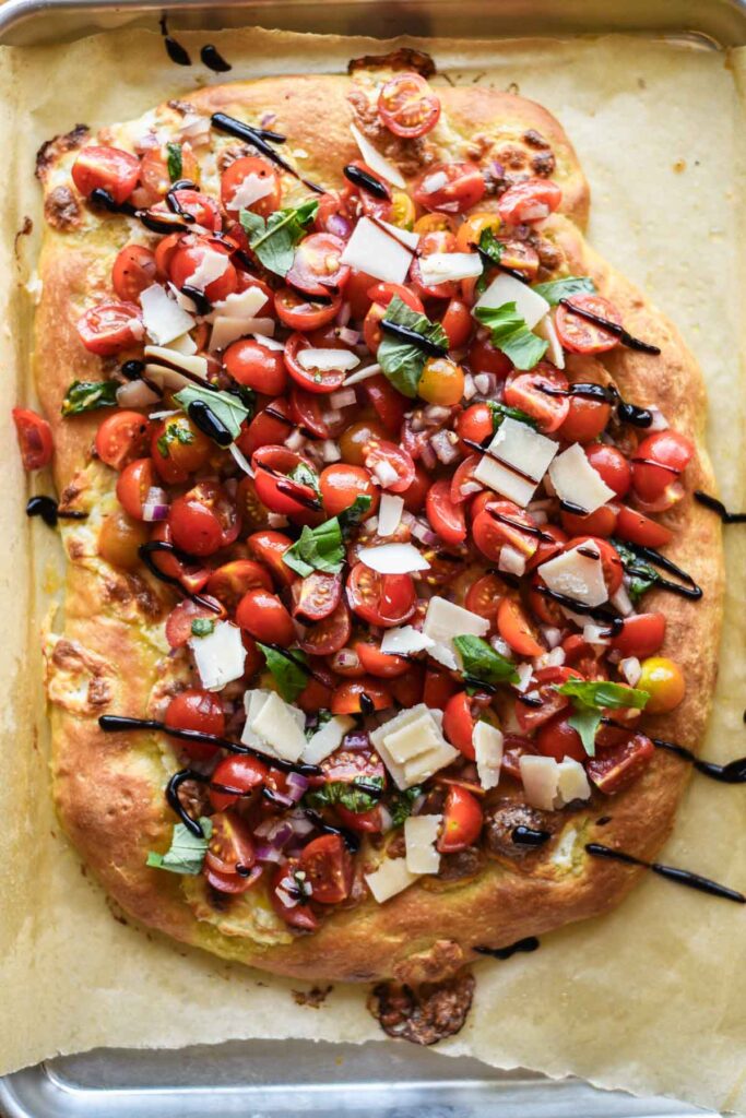 Finished pizza topped with bruschetta, balsamic glaze and shaved parmesan cheese.