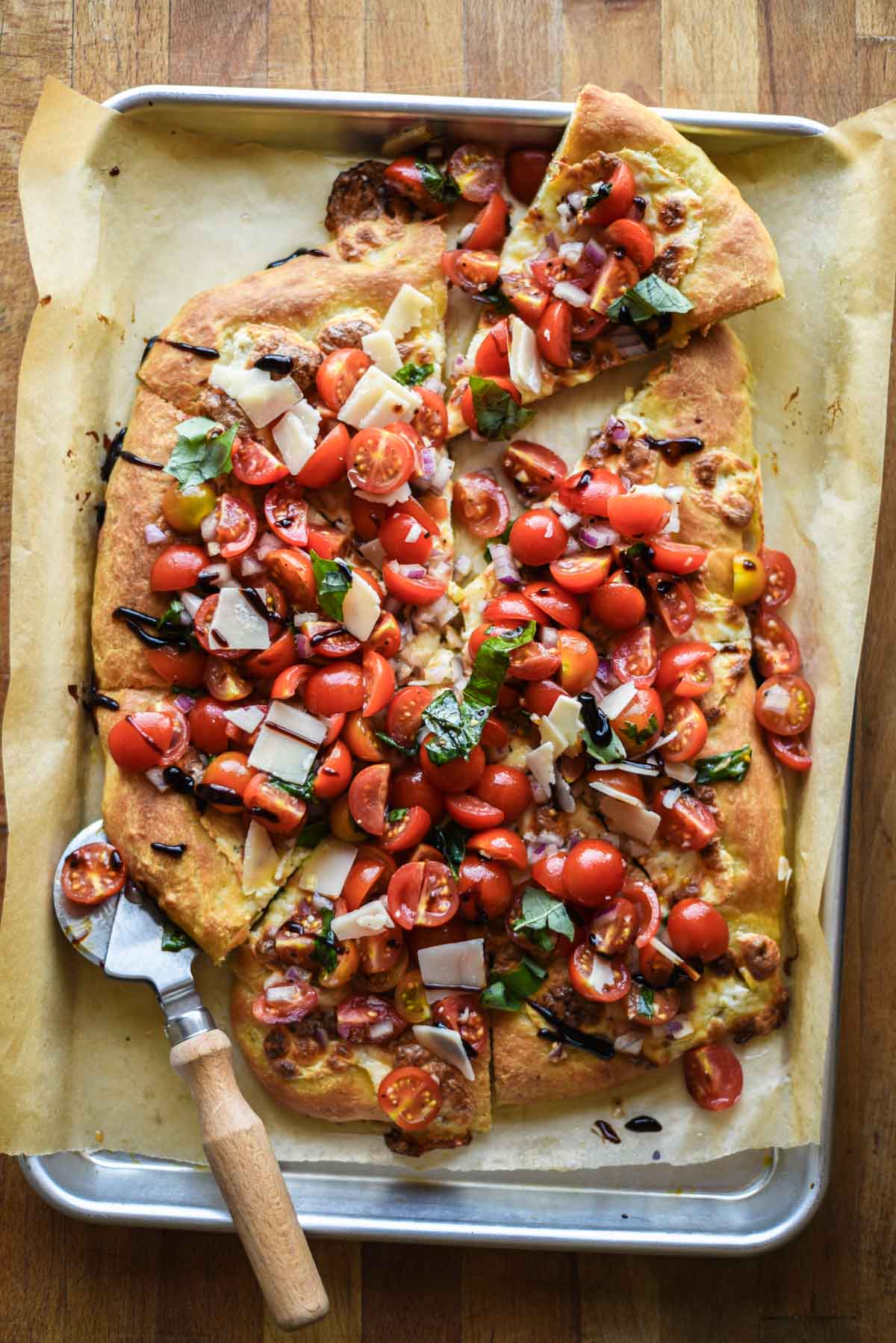 Pizza sliced into on a baking sheet with a wood handled pizza cutter.