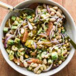 white bean citrus salad in a serving bowl with two serving spoons.