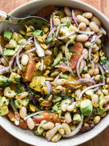 white bean citrus salad in a serving bowl with two serving spoons.